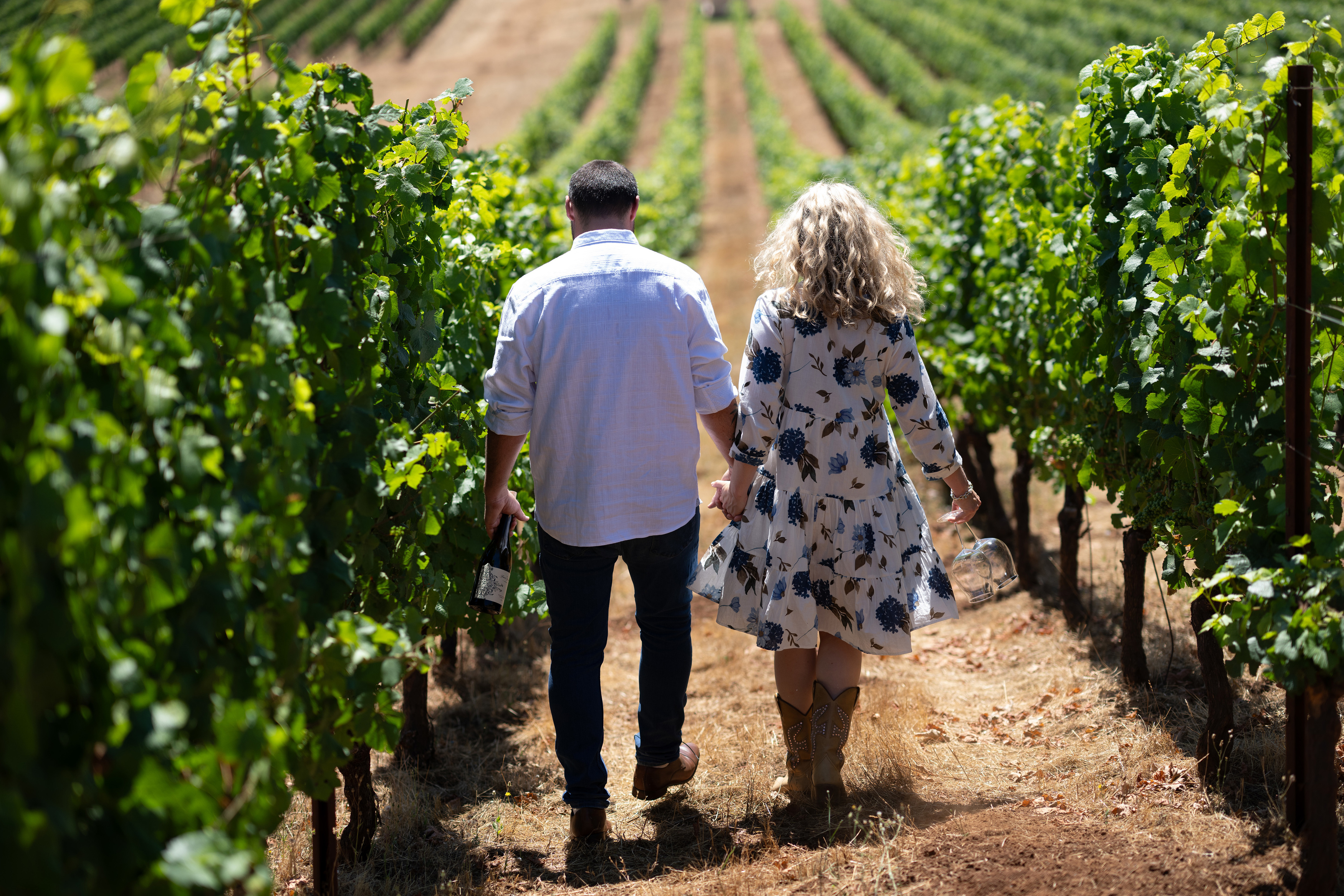 a man and woman holding hands walking in a vineyard